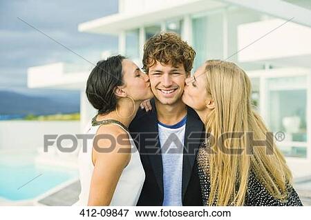 Stock Photo - Women kissing man's cheeks outdoors. Fotosearch