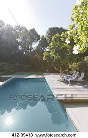 Stock Image - Wooden deck and lounge chairs by swimming pool. Fotosearch