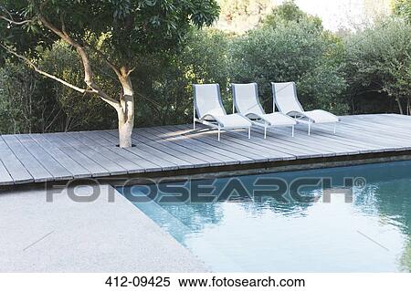 Stock Photography - Wooden deck and lounge chairs by swimming pool. Fotosearch