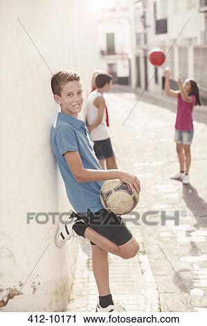 Stock Image - Boy holding soccer ball in alley. Fotosearch