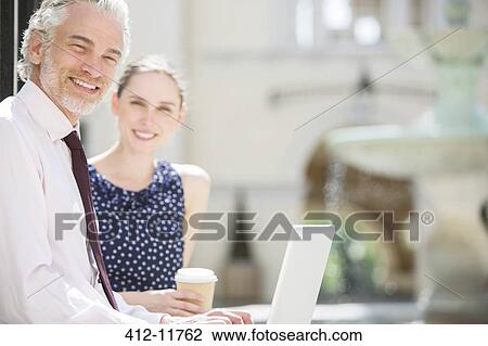 Stock Image - Business people using laptop outdoors. Fotosearch