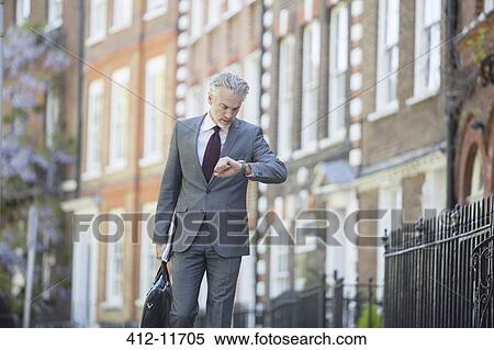 Stock Photography - Businessman checking wristwatch on urban sidewalk. Fotosearch