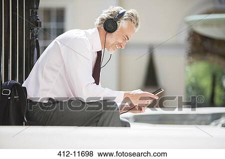Businessman listening to headphones on city street View Large Photo Image Stock Photo - Businessman listening to headphones on city street. Fotosearch