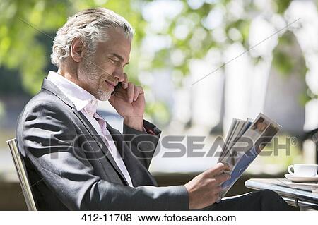 Stock Photo - Businessman reading magazine at sidewalk cafe. Fotosearch
