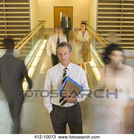 Businessman standing in busy office corridor View Large Photo Image Stock Image - Businessman standing in busy office corridor. Fotosearch