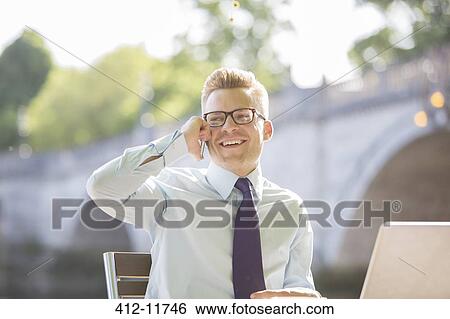 Stock Photograph - Businessman talking on cell phone at sidewalk cafe. Fotosearch