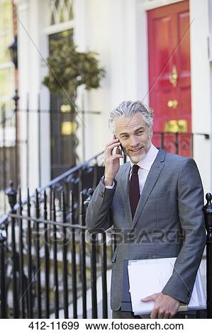 Stock Photo - Businessman talking on cell phone on front stoop. Fotosearch