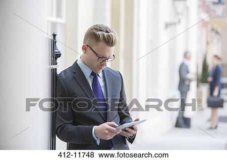 Businessman using digital tablet on city sidewalk View Large Photo Image Stock Photo - Businessman using digital tablet on city sidewalk. Fotosearch