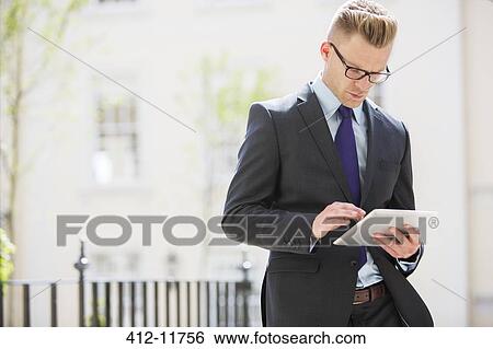 Stock Photograph - Businessman using digital tablet on city street. Fotosearch