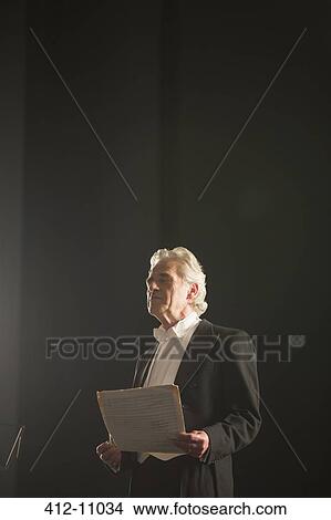 Picture - Calm orchestra conductor holding sheet music with eyes closed. Fotosearch