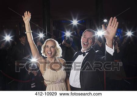 Stock Photo - Celebrity couple waving on red carpet with paparazzi in background. Fotosearch