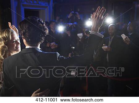 Stock Image - Celebrity couple waving to paparazzi at red carpet event. Fotosearch