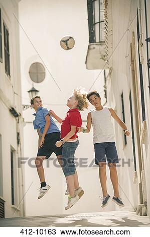 Stock Image - Children playing with soccer ball in alley. Fotosearch