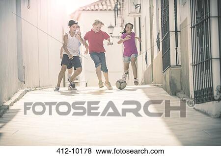 Stock Photo - Children playing with soccer ball in alley. Fotosearch