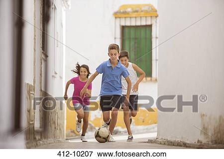 Stock Photo - Children playing with soccer ball in alley. Fotosearch