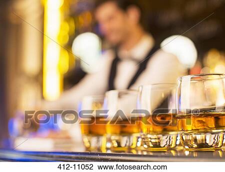 Stock Image - Close up of bourbon in glasses in a row on bar. Fotosearch
