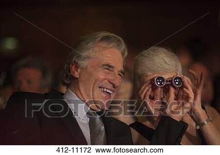 Stock Image - Close up of smiling couple using opera glasses in theater audience. Fotosearch