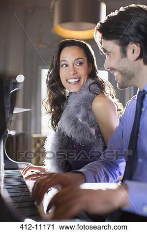 Stock Image - Close up of well dressed couple playing piano in lounge. Fotosearch