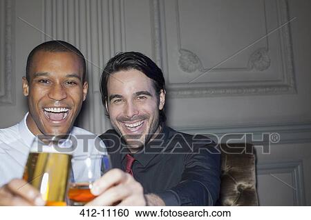 Stock Image - Close up portrait of smiling men toasting beer and cocktail. Fotosearch
