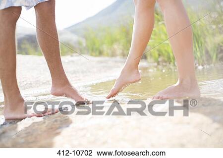 Stock Image - Couple dipping feet in rural pond. Fotosearch