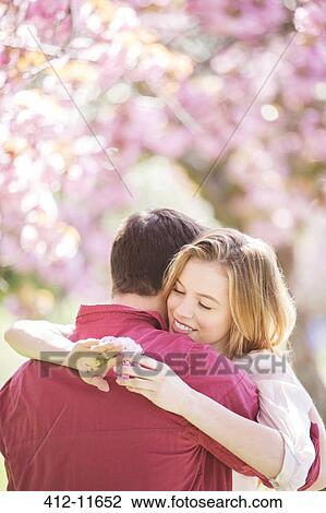 Stock Image - Couple hugging under tree with pink blossoms. Fotosearch