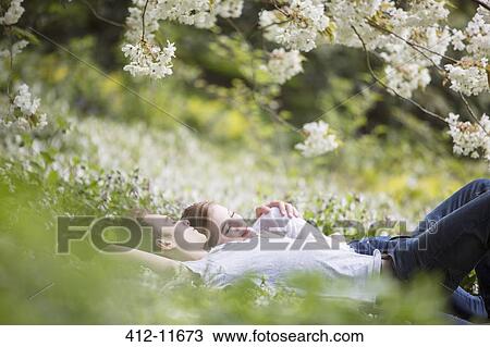Stock Image - Couple laying in grass under tree with white blossoms. Fotosearch