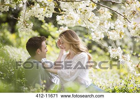 Stock Image - Couple relaxing in grass under tree with white blossoms. Fotosearch