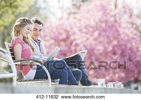 Stock Image - Couple relaxing together on park bench. Fotosearch
