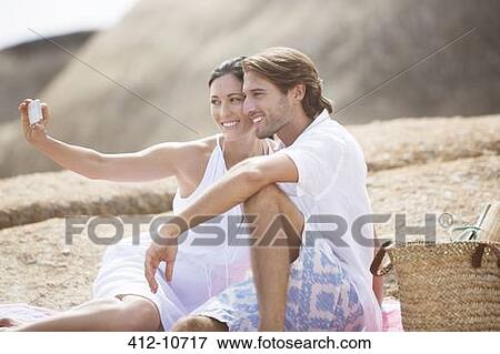 Stock Photo - Couple taking pictures together on sandy beach. Fotosearch