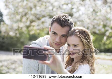 Couple taking self-portrait in park View Large Photo Image Stock Photo - Couple taking self-portrait in park. Fotosearch