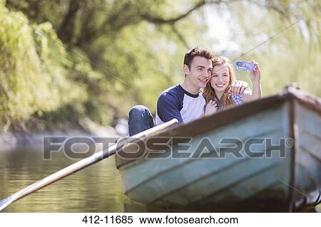 Couple taking self-portraits in rowboat View Large Photo Image Stock Photography - Couple taking self-portraits in rowboat. Fotosearch