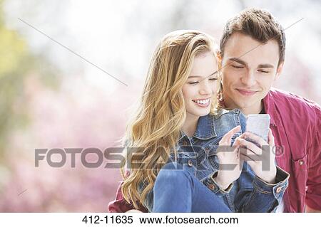 Couple using cell phone outdoors View Large Photo Image Stock Photography - Couple using cell phone outdoors. Fotosearch