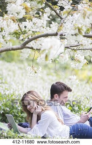 Couple using digital tablet and cell phone in park View Large Photo Image Stock Image - Couple using digital tablet and cell phone in park. Fotosearch