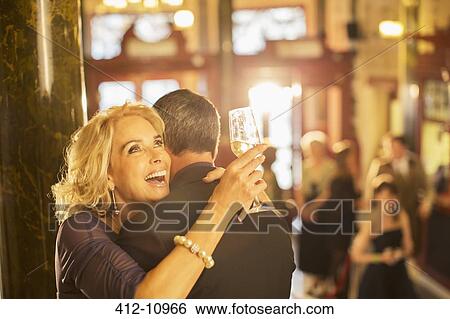 Stock Photograph - Enthusiastic woman with champagne hugging man in theater lobby. Fotosearch