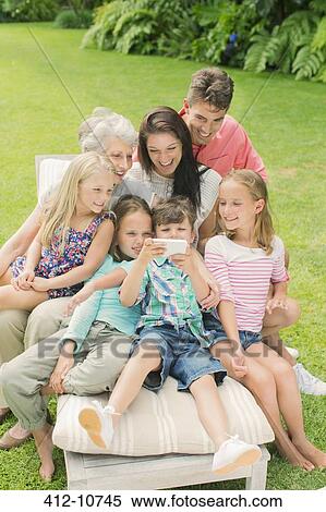 Stock Photography - Family using cell phone together in backyard. Fotosearch