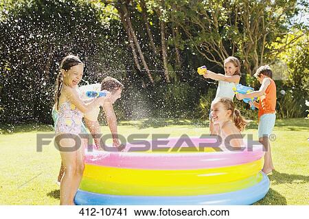 Stock Image - Father and children playing with water guns in backyard. Fotosearch