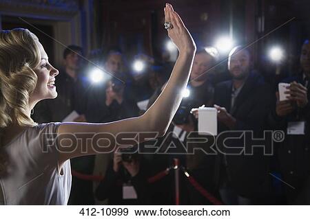 Stock Photo - Female celebrity waving to paparazzi at red carpet event. Fotosearch