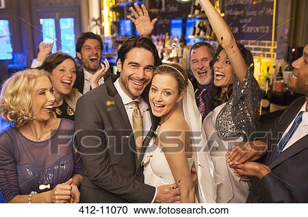 Stock Image - Friends cheering around smiling bride and groom at wedding reception. Fotosearch