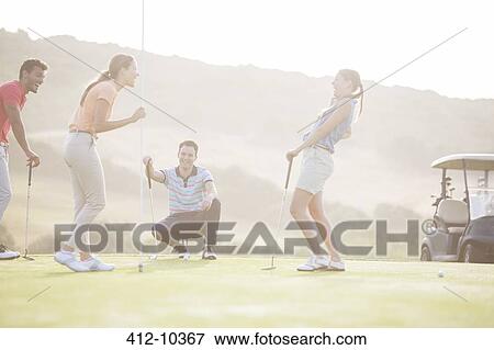 Stock Photo - Friends laughing near hole on golf course. Fotosearch
