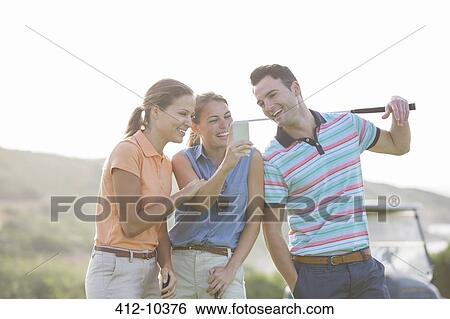 Friends looking at cell phone on golf course View Large Photo Image Stock Photograph - Friends looking at cell phone on golf course. Fotosearch