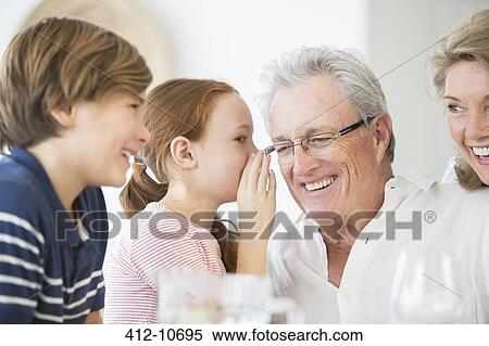 Stock Photography - Girl whispering to grandfather at table. Fotosearch