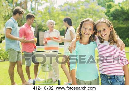 Stock Image - Girls hugging at backyard barbecue. Fotosearch