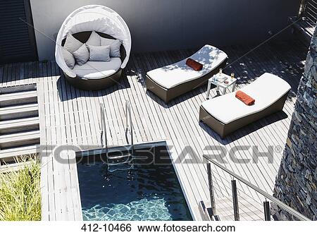 Lounge chairs on wooden deck by modern pool View Large Photo Image Stock Photograph - Lounge chairs on wooden deck by modern pool. Fotosearch