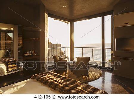 Stock Image - Luxury bedroom overlooking ocean at sunset. Fotosearch