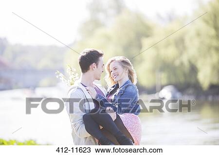 Stock Image - Man carrying girlfriend along river. Fotosearch
