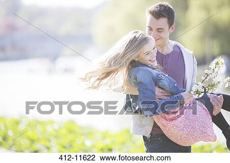 Stock Image - Man carrying girlfriend outdoors. Fotosearch