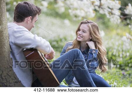 Stock Photo - Man playing guitar for girlfriend outdoors. Fotosearch