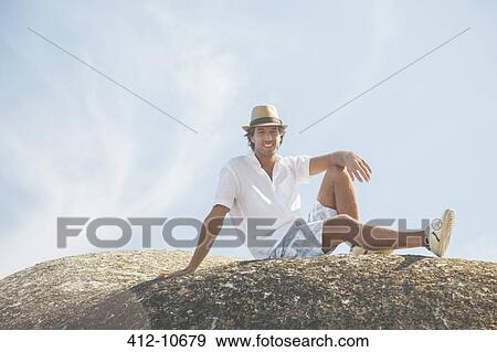 Stock Photo - Man sitting on rock formation. Fotosearch