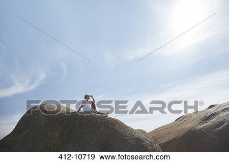 Stock Photo - Man sitting on rock formation. Fotosearch