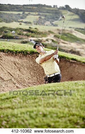 Stock Image - Man swinging from sand trap on golf course. Fotosearch